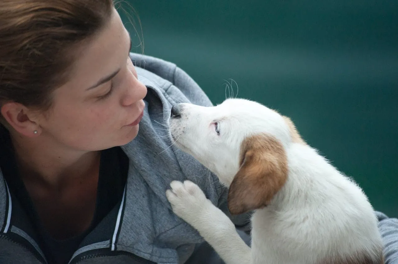A woman holding a white puppy close to her face
